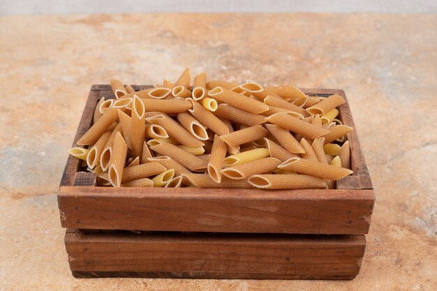 Heap of raw pasta in a wooden basket on marble background. High quality photo