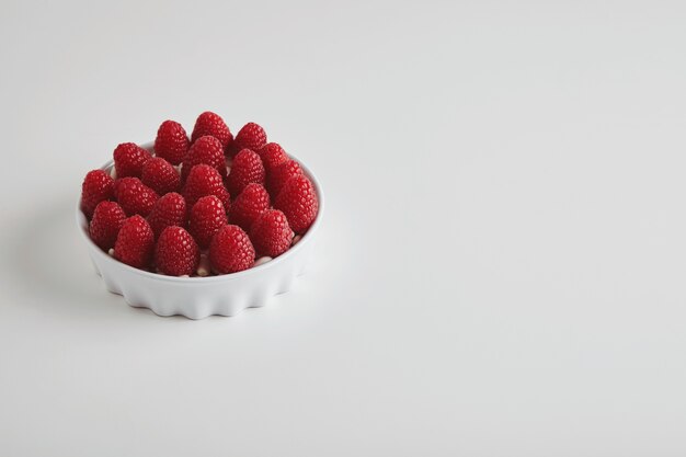 Heap of ripe raspberries accurately placed in ceramic bowl isolated on white table