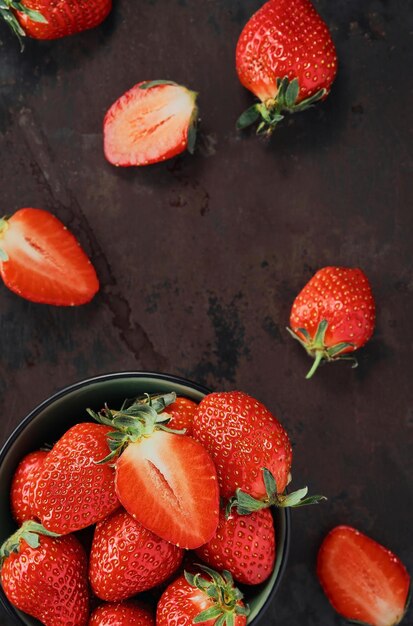 Heap of ripe strawberries in dark plate on old metal background with copy space Top view point vertical frame