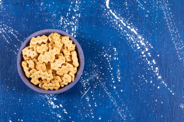 Heap of salty small crackers placed in blue bowl