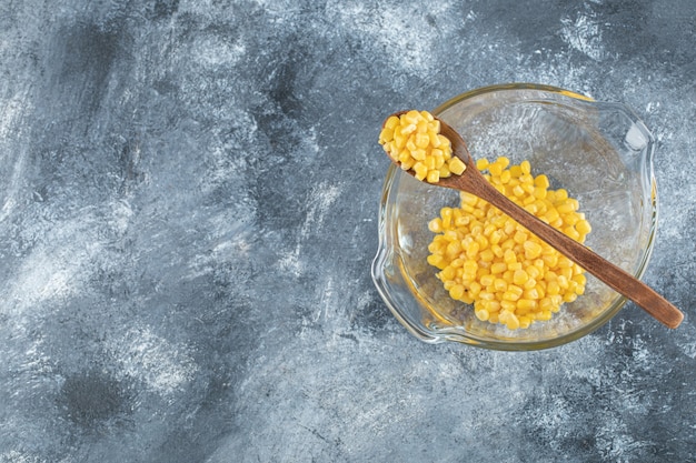 Heap of sweet corns in glass bowl with wooden spoon.