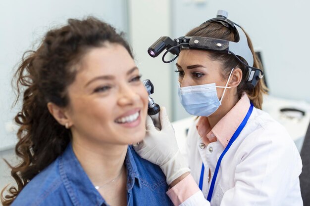 Проверка слуха Врач-отоларинголог проверяет ухо женщины с помощью отоскопа или аурископа в медицинской клинике