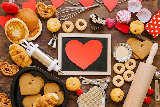 Heart and chalkboard near bakeware and pastry