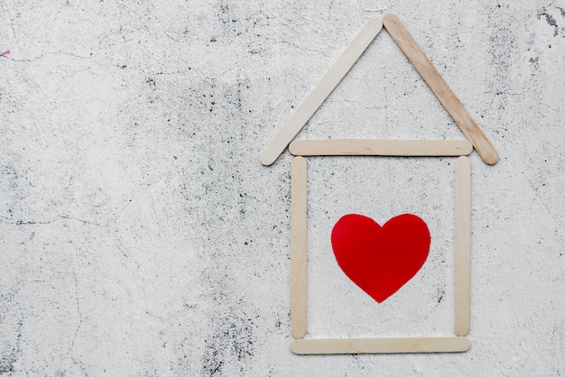 Free photo heart inside the house shape made with ice-cream sticks on white weathered wall