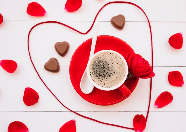 Foto gratuita cuore di nastro vicino al cioccolato dolce caramelle, tazza di bevanda sul piatto e petali