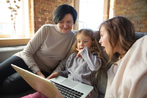 Heart's warming. Happy loving family. Grandmother, mother and daughter spending time together. Watching cinema, using laptop, laughting. Mother's day, celebration, weekend, holiday childhood concept.