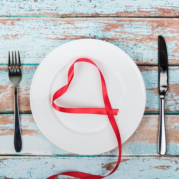 Форма сердца из красной ленты на тарелке со столовыми приборами