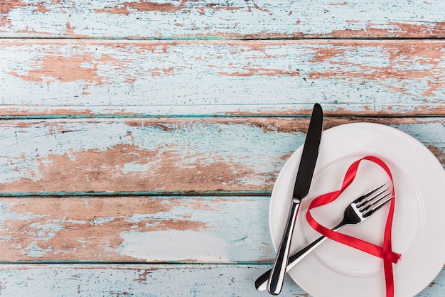 Heart shape from ribbon on plate with cutlery on table 