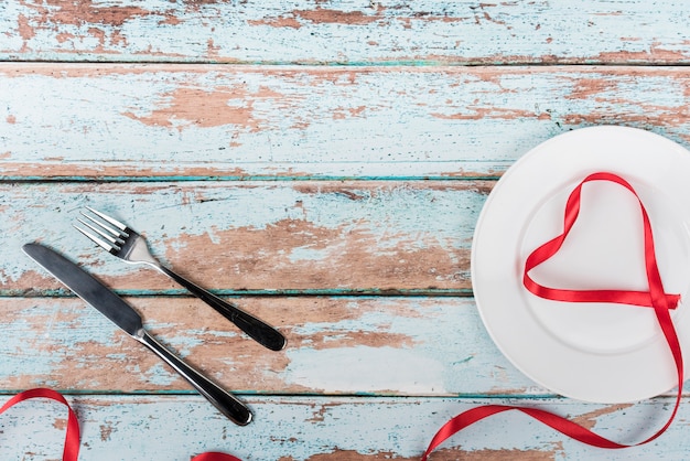 Heart shape from ribbon on plate with cutlery 