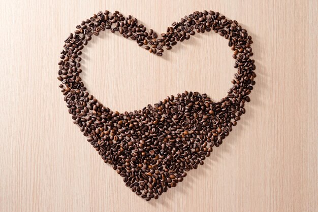 木製の背景にコーヒー豆で作られたハートの形 Premium写真