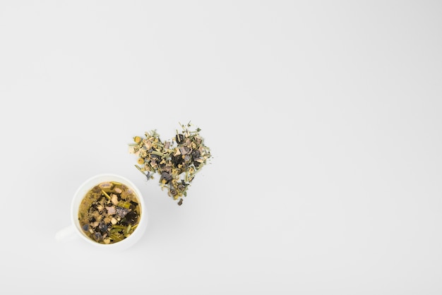 Heart shape made up of herb near cup of tea on white backdrop