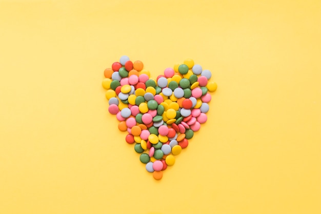 Heart shape made with gems candies on yellow backdrop