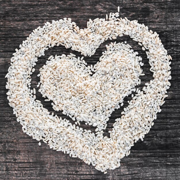 Heart shape made with uncooked white rice on wooden backdrop