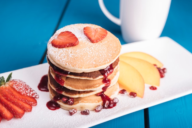 Fetta della fragola di figura del cuore sopra la pila di pancake sopra la tabella blu