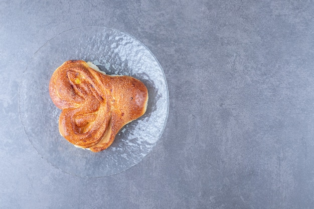 Heart shaped bun on the glass plate on marble table.