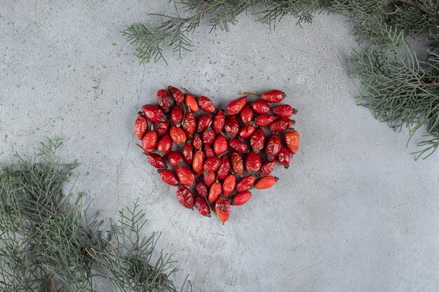 Heart-shaped bundle of dog-rose and branches on marble surface