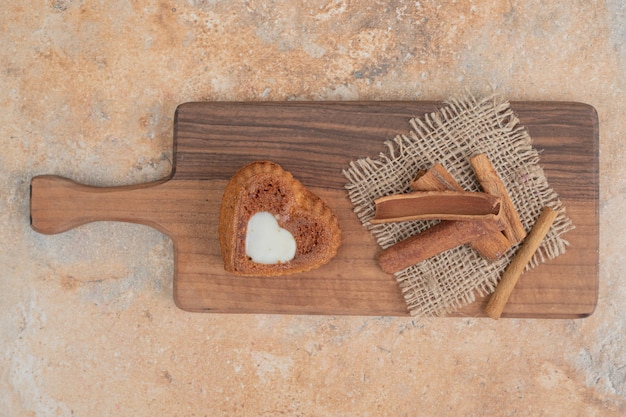 Heart shaped cake and cinnamon sticks on wooden board. 