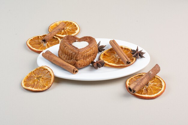 Heart shaped cake with orange slices, cloves and cinnamon on white plate