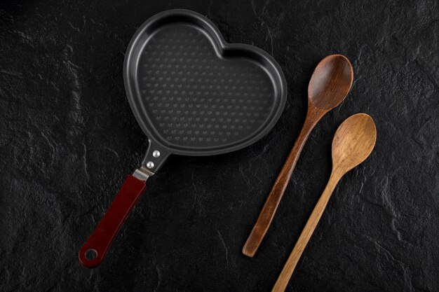 Heart shaped pan and wooden spoon on black surface