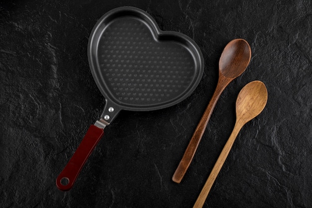 Heart shaped pan and wooden spoon on black surface