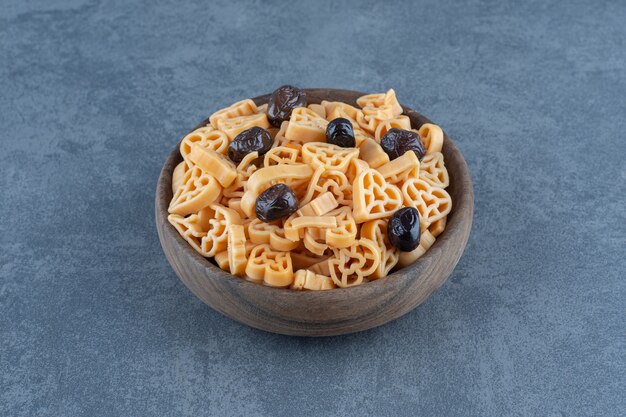 Heart shaped pasta with olives in wooden bowl. 