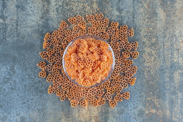 Free photo heart shaped pastas in and around the bowl, on the marble background.