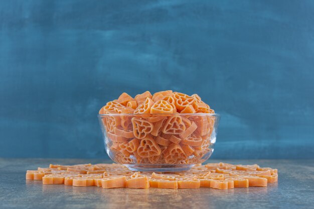 Heart shaped pastas in and around the bowl, on the marble surface.