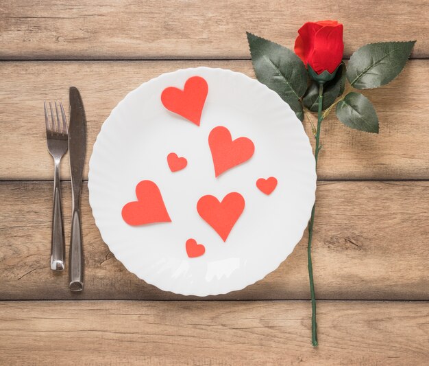 Hearts on plate between cutlery and flower 