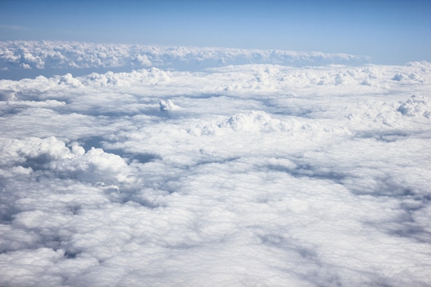 Тяжелые белые / серые облака из вида на самолет, с голубым небом и солнечным светом, самолет летит над облаками