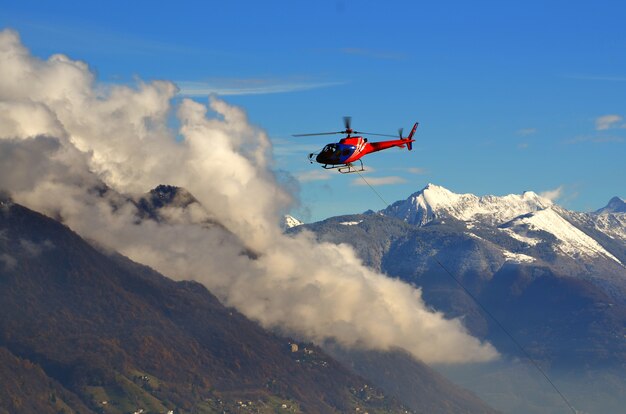 Вертолет летит среди облаков над заснеженными горами