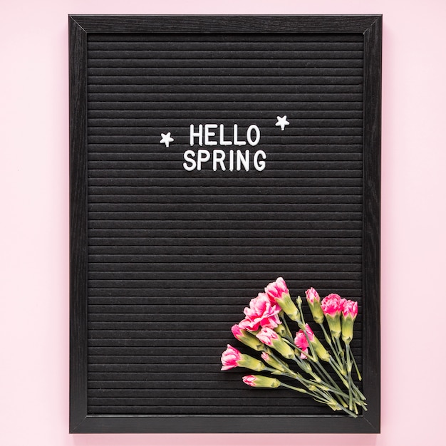 Free photo hello spring inscription with pink flowers on black board