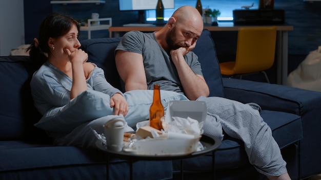 Helpless unhappy, depressed, frustrated young couple sitting in couch suffering from insomnia, stress anxiety, mental problems, suicidal thoughts, chronic disease. People looking lost into space