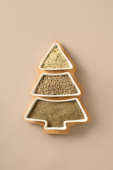 Hemp seeds, flour, kernels in plate shape of christmas tree isolated on beige background. xmas vertical eco greeting card. view from above. food holiday concept. alternative creative xmas tree.