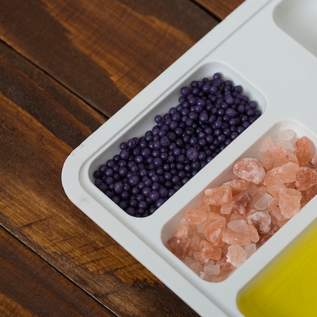 Herbal rock salt; oil and blueberry cosmetics products on white plate over the wooden desk