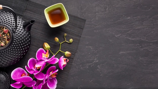 Herbal tea and beautiful orchid flower on black place mat over slate stone backdrop