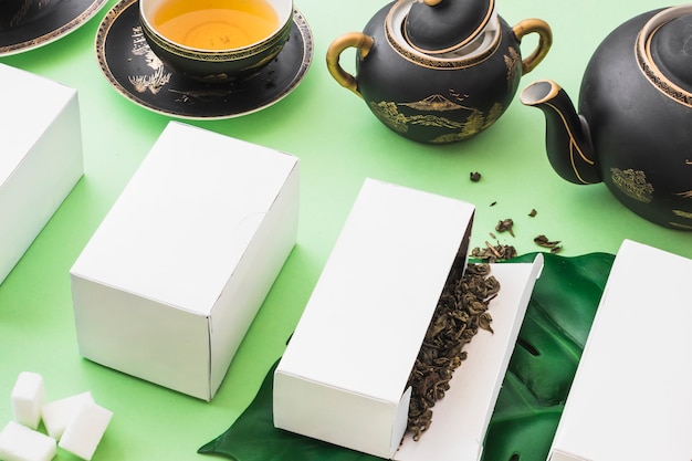 Herbal tea boxes with tea and sugar cubes on green backdrop