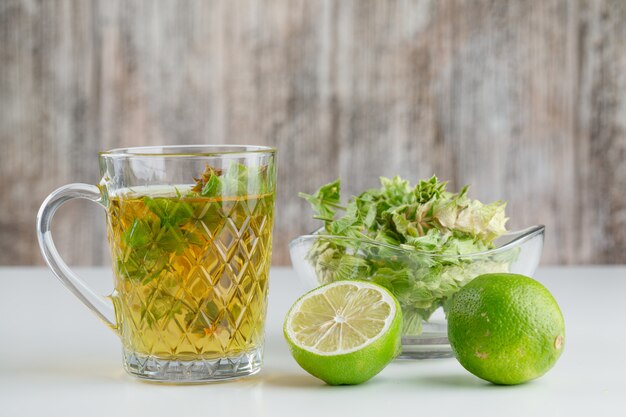 Herbal tea in a glass cup with herbs, limes side view on white and grungy