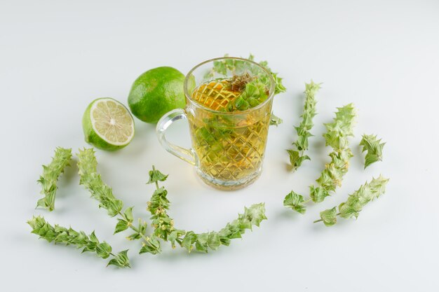 Травяной чай в стеклянной чашке с листьями, лайм под высоким углом зрения на белом