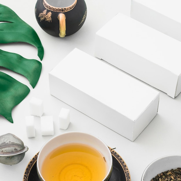 Herbal tea, sugar cubes, tea strainer and white boxes on backdrop