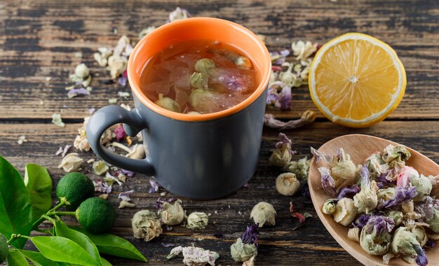 Herbal tea with dried flowers, lemon, limes in a cup on wooden surface