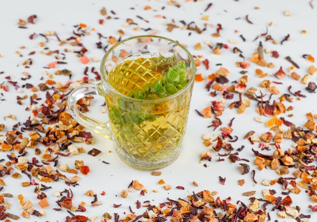 Herbal tea with dried herbs in a glass cup on white, high angle view.