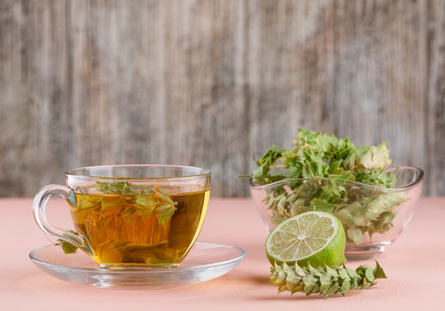 Free photo herbal tea with herbs, lime in a glass cup on pink and wooden,