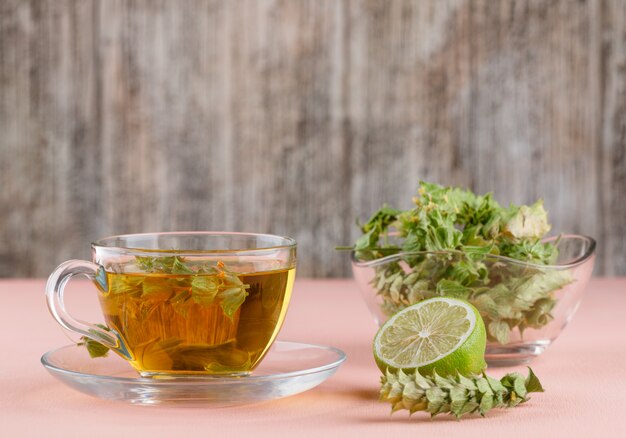 Травяной чай с зеленью, лайм в стеклянной чашке на розовом и деревянном,