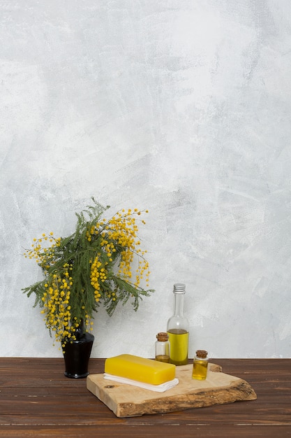Травяное желтое мыло на сложенной салфетке и флакон с эфирным маслом рядом с желтой вазой с мимозой