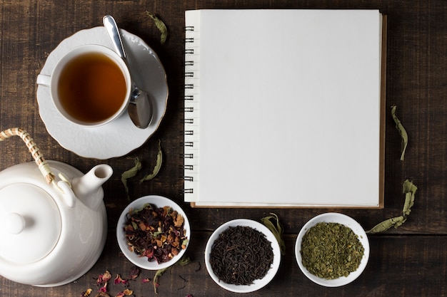 Herbs tea with teapot and blank spiral notebook on wooden table