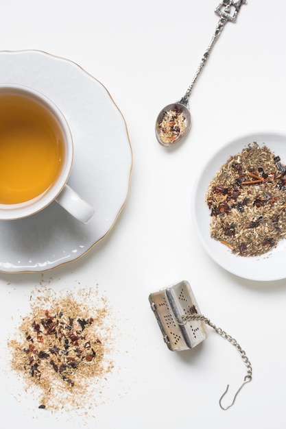 Herbs with tea cup; spoon and strainer on white backdrop