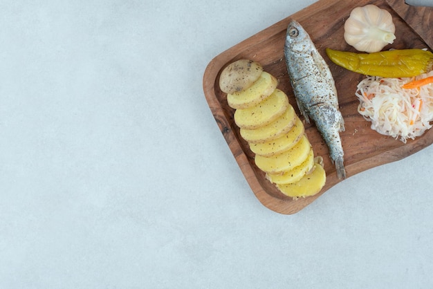 Herring, boiled potatoes and mixed pickles on wooden board.