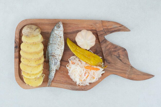 Herring, boiled potatoes and mixed pickles on wooden board.