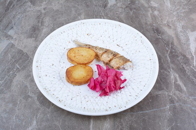 Herring rolls, potato and red cabbage on white plate.