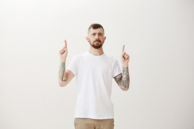 Hesitant and awkward hipster guy looking unsure and pointing fingers up at promo